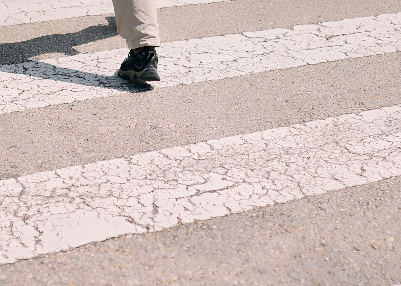 Person walking across a crosswalk with their feet in the air, wearing cream-colored pants and black shoes